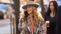 Carrie, gespielt von Sarah Jessica Parker, telefoniert am Handy. Sie trägt einen blau-beige-karrierten Mante und einen farblich perfekt abgestimmt Hut. Eben Carrie.