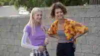 Hunter Schafer und Zendaya stehen entspannt und lächelnd vor einer Mauer
