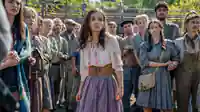 Während Lucy (Rachel Zegler) mitten in der Menschenmenge steht, schauen alle geschockt nach vorne, weil ihr Name gezogen wurde.