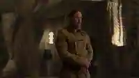 Szenenbild aus der Serie "Dune: Prophecy": Desmond Hart, gespielt von Travis Fimmel, steht in einem schwach beleuchtetem Raum. Er trägt einen langen beige-farbenen Mantel.