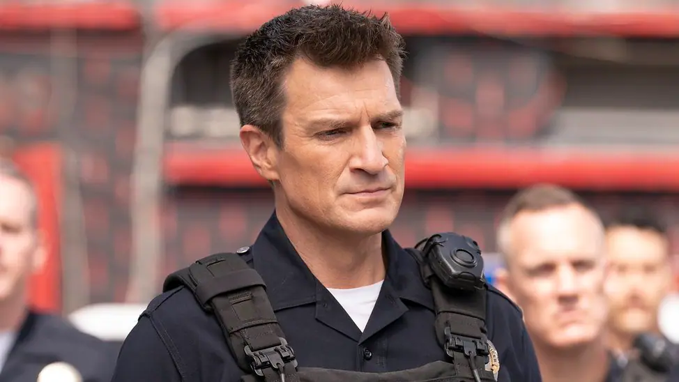 Nolan in Uniform, offenbar bei einer Besprechung. Im Hintergrund stehen Kollegen.