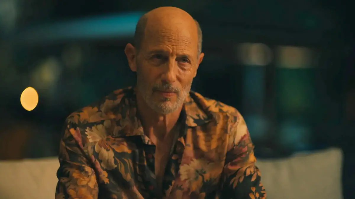 Szene aus der HBO-Serie The White Lotus: Glatzköpfiger Mann in einem floralen Hemd sitzt nachts draußen.