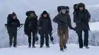 Ellie, gespielt von Bella Ramsey; Joel, gespielt von Pedro Pascal; und 3 weiter Überlebenden laufen im Schneesturm mit Gewähren durch die verschneite Winterlandschaft.