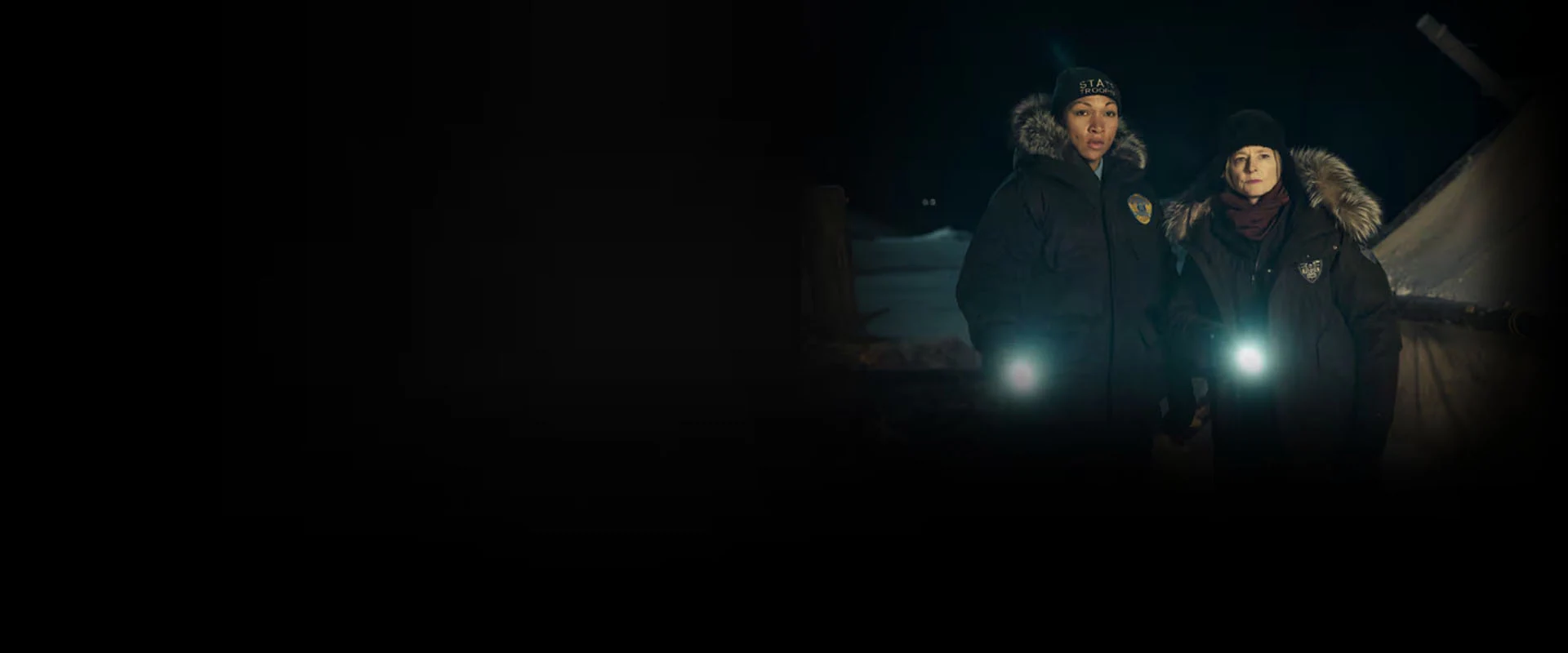 Immagine Promozione True Detective: Night Country su NOW con Jodie Foster e Kali Reis in giacche invernali che tengono torce accese su uno sfondo notturno